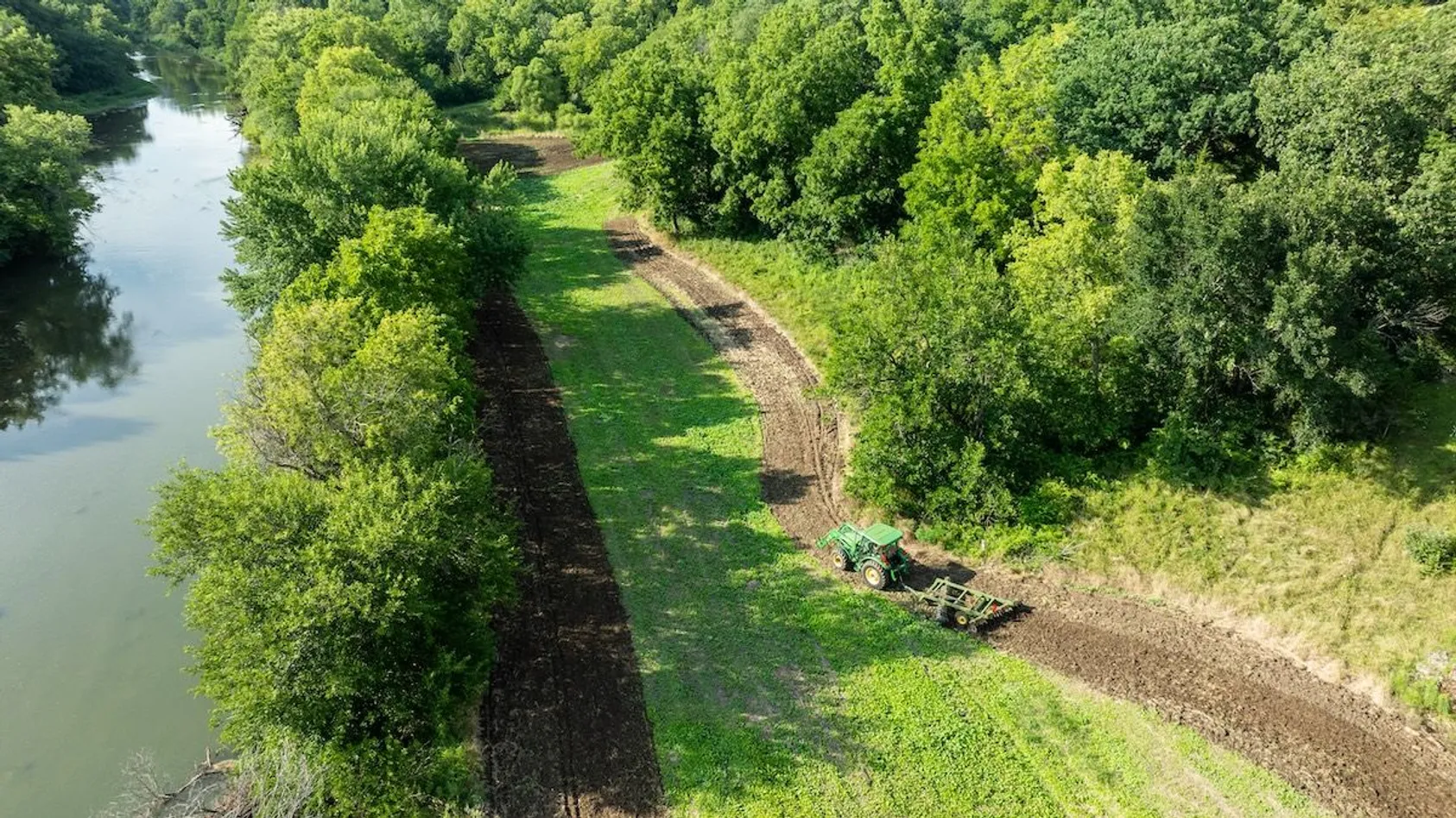 Scenic aerial view of meandering creek or river flowing through green agricultural fields and wooded areas, showing natural water features