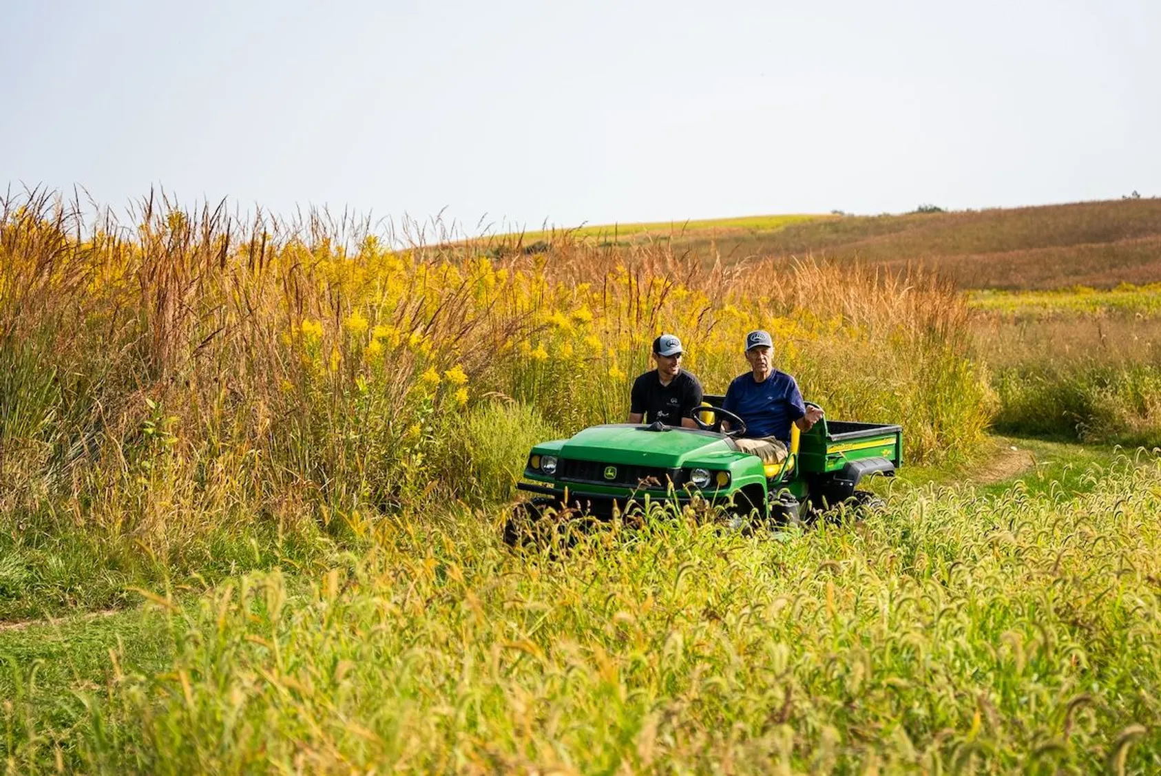 Two men standing beside green utility vehicle (UTV) in tall grass field, demonstrating hands-on land evaluation and field experience