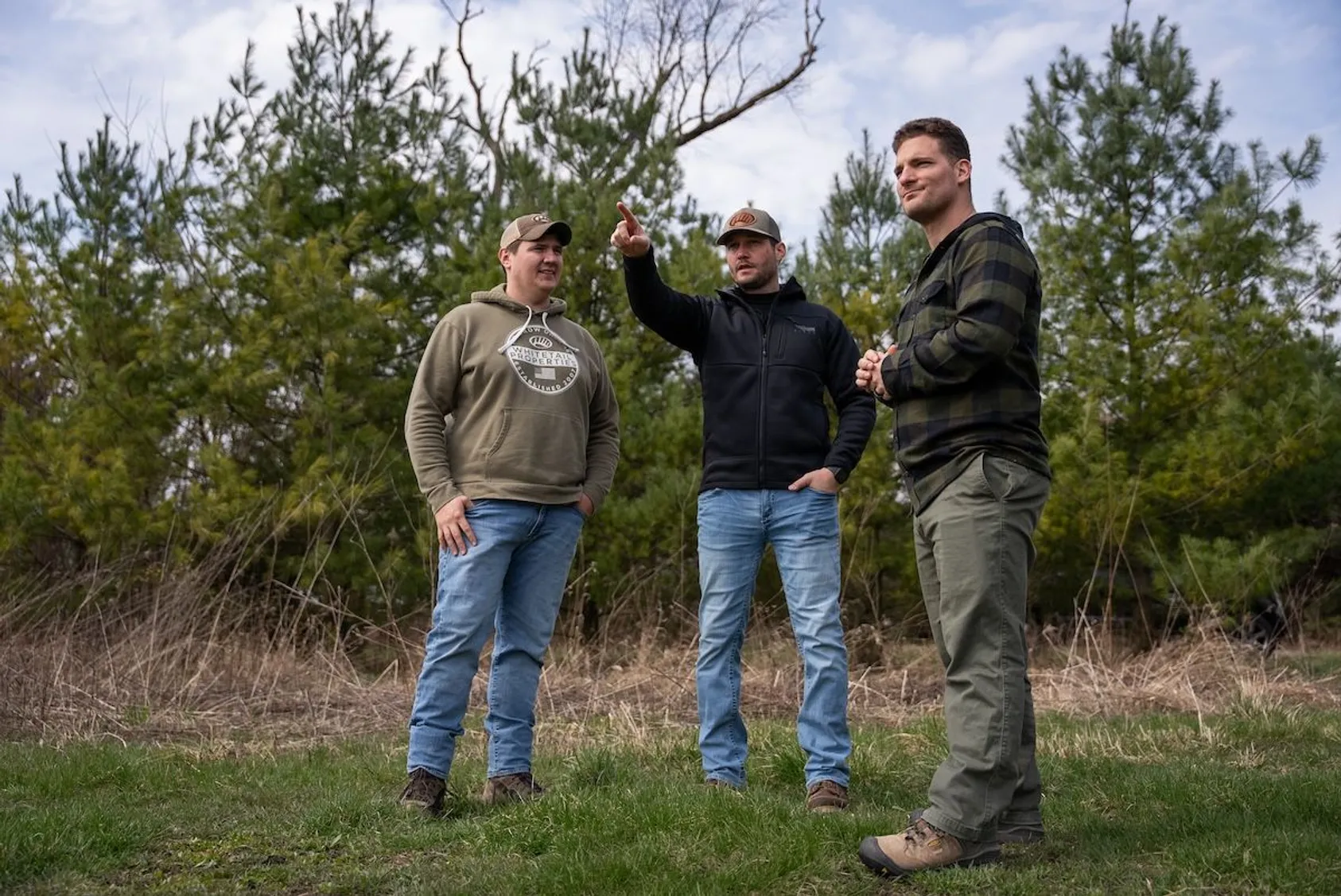 Group of four men standing together outdoors in rural setting with trees in background, representing networking and teamwork in land real estate industry