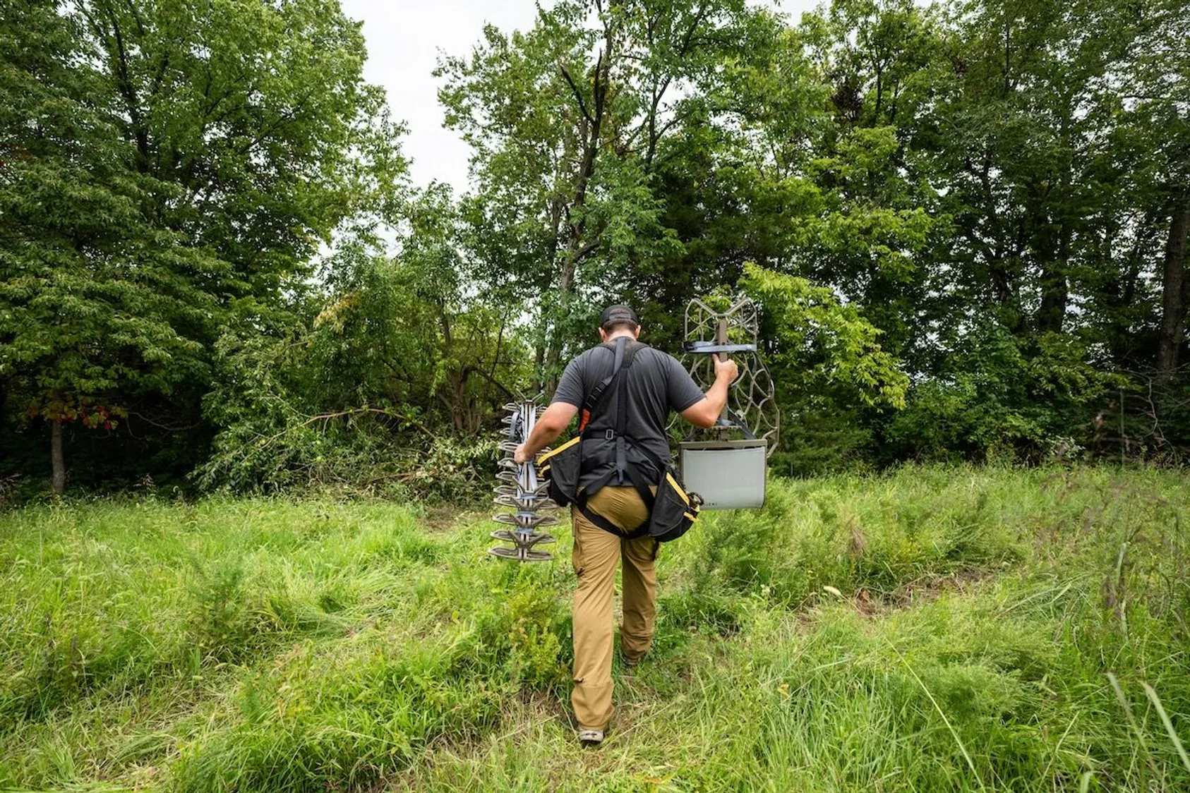 Person using surveying equipment in wooded area, demonstrating technical expertise and precision tools used in land evaluation and boundary determination