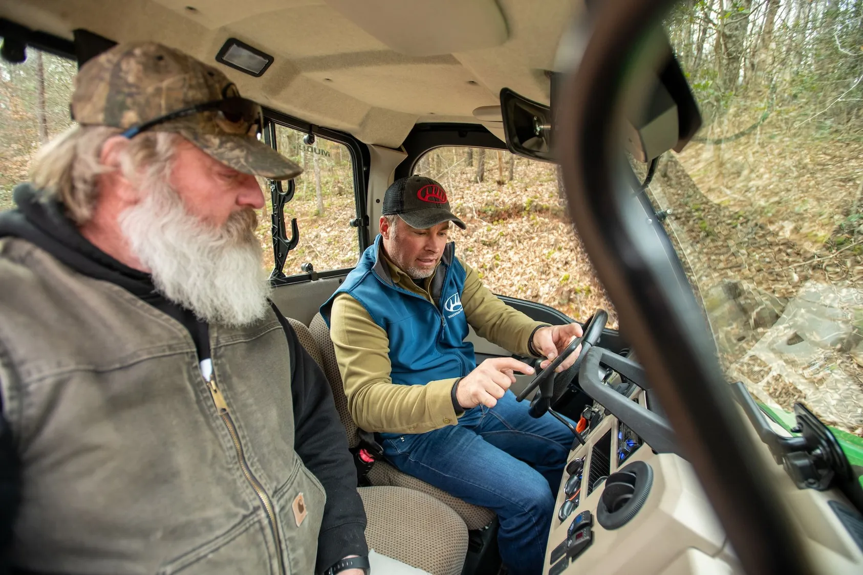 Two men sitting in utility terrain vehicle in wooded area, representing property inspection and land management activities for rural property owners