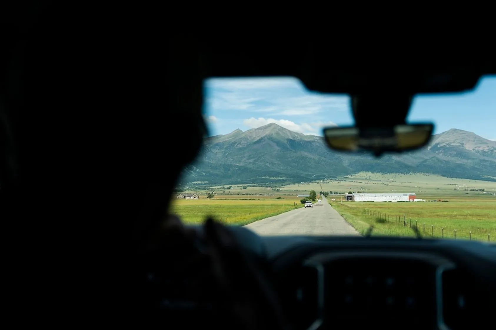 View through car windshield of rural landscape with mountains and farmland, showing the perspective of someone looking for land to purchase