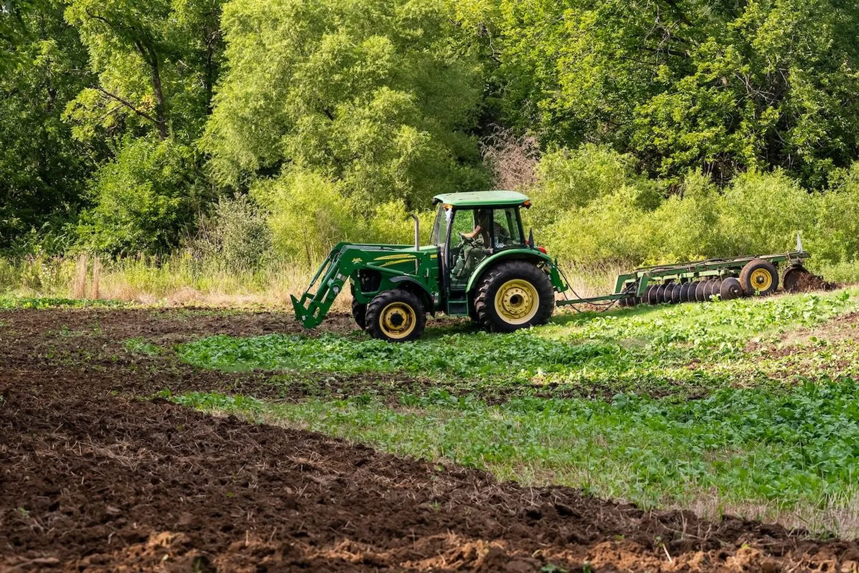 Green tractor working in field for habitat improvement, demonstrating equipment needed for food plot establishment and land management