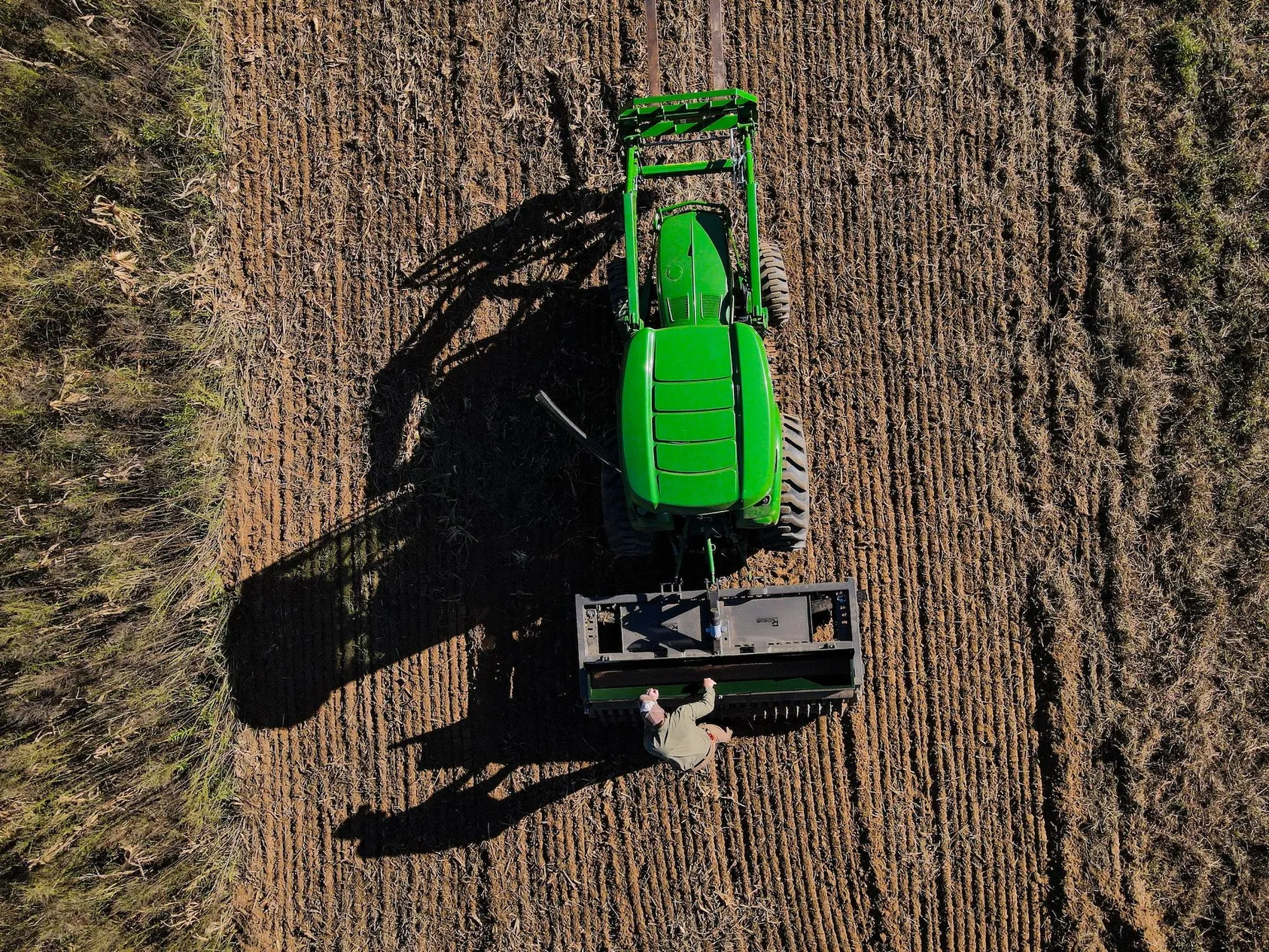 Large green agricultural tractor working in plowed field, demonstrating modern farming operations and equipment used on valuable farmland