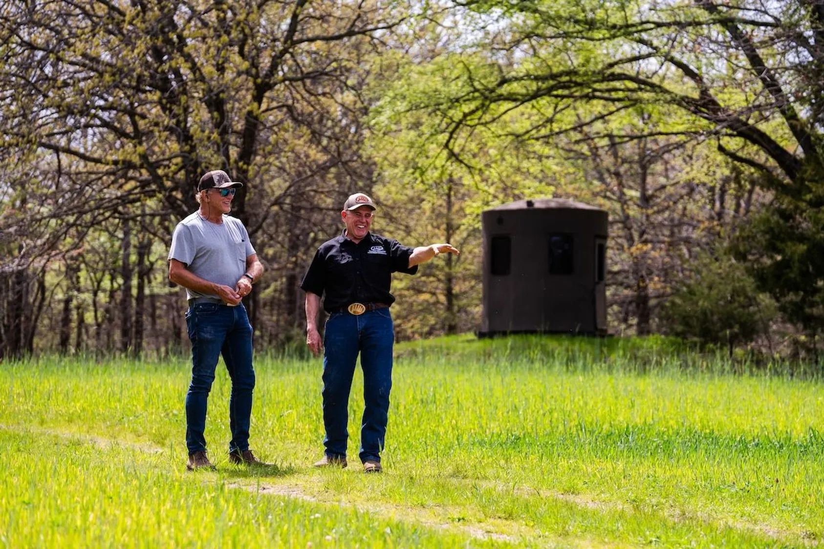 Two men in business attire standing in grassy field with trees in background, representing land professionals discussing property opportunities