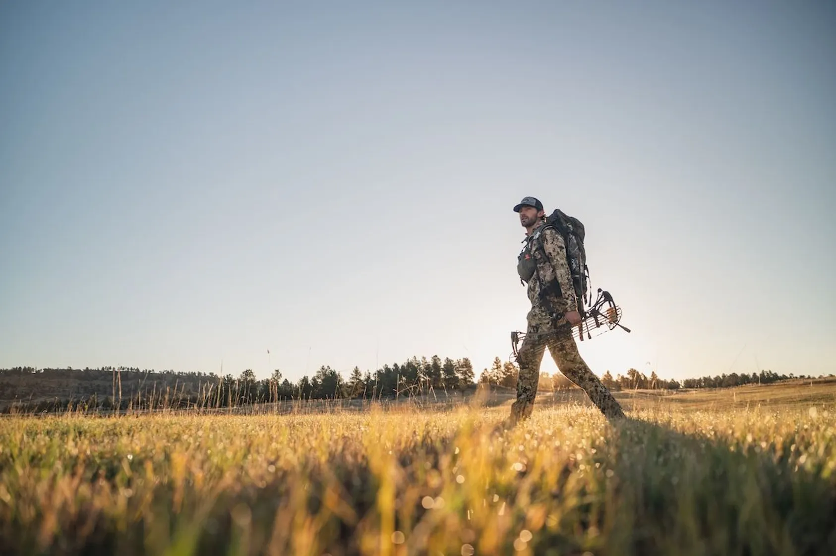 Hunter in camouflage walking through tall grass field with hunting equipment, demonstrating recreational hunting opportunities on rural land