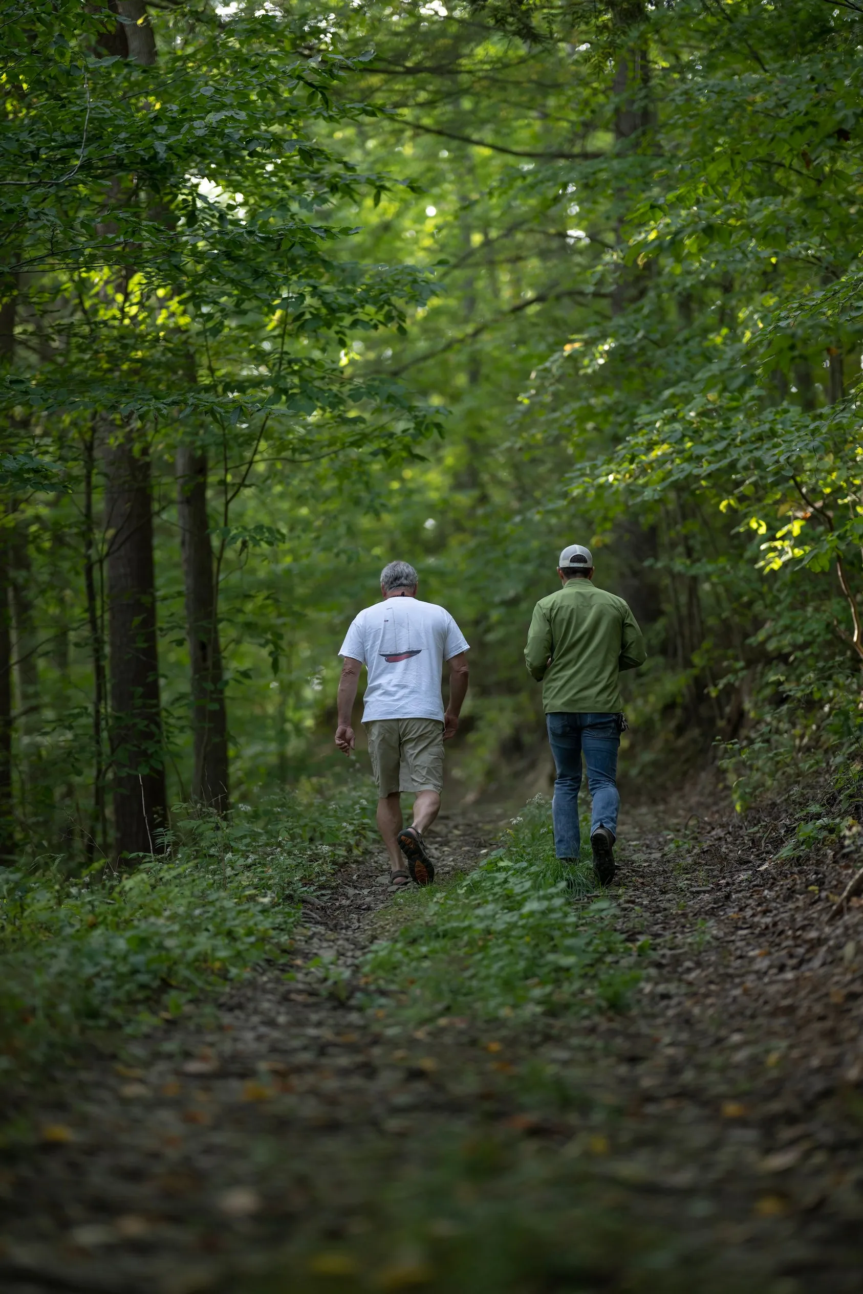 Two men walking along wooded trail path surrounded by lush green forest, demonstrating property inspection and land assessment process