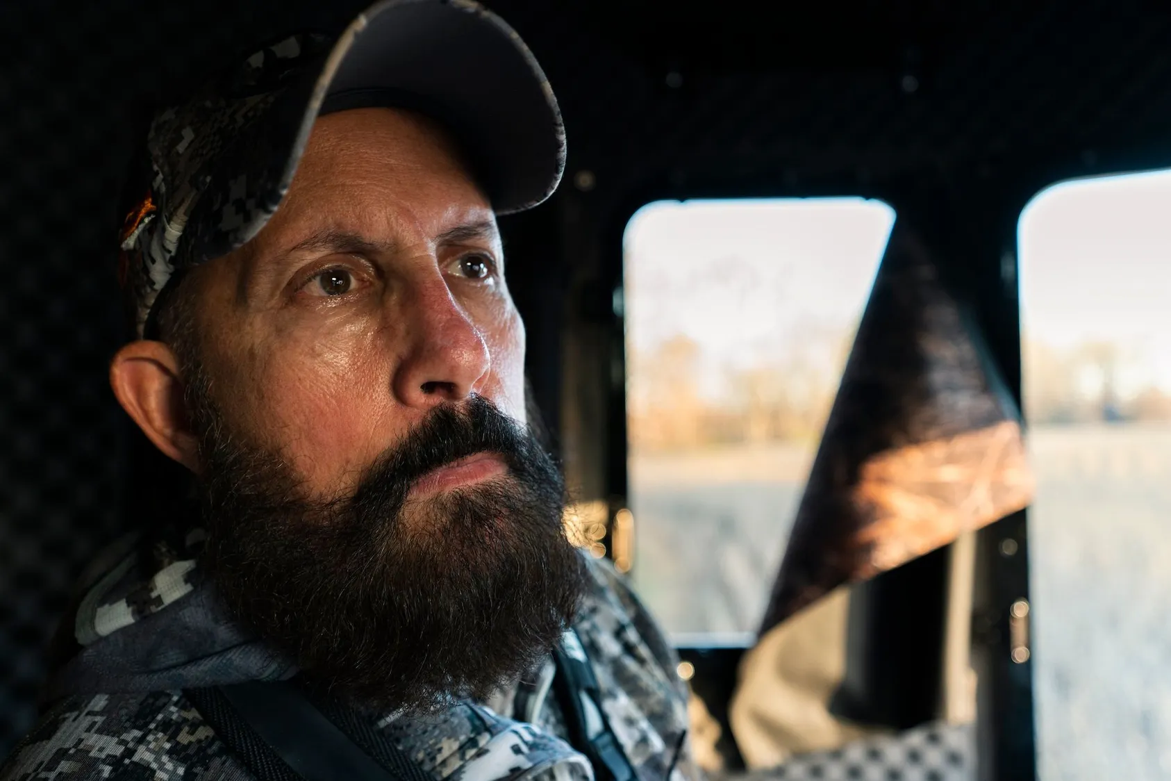 Bearded man in cap sitting inside vehicle cab looking thoughtful, representing real estate investor or land buyer considering investment strategies