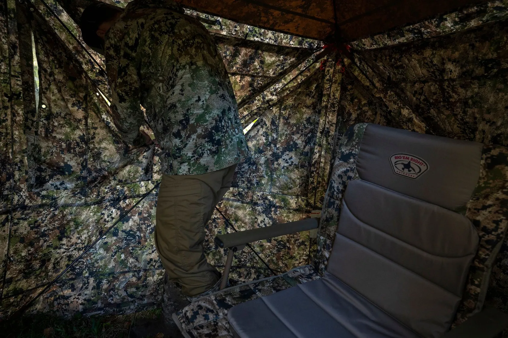 Hunter in full camouflage gear crouched in forest setting with hunting equipment, positioned for turkey hunting