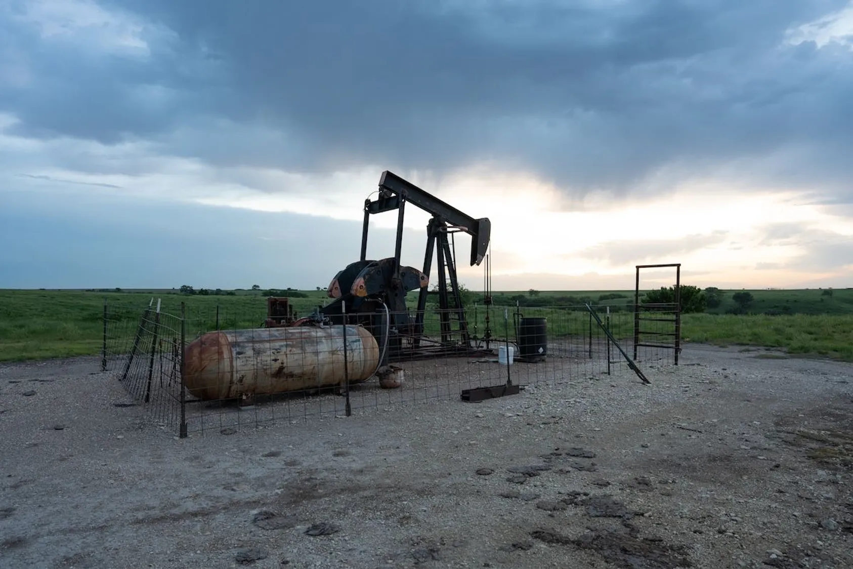 Oil pump jack (nodding donkey) on rural land with green fields in background, showing active mineral extraction equipment