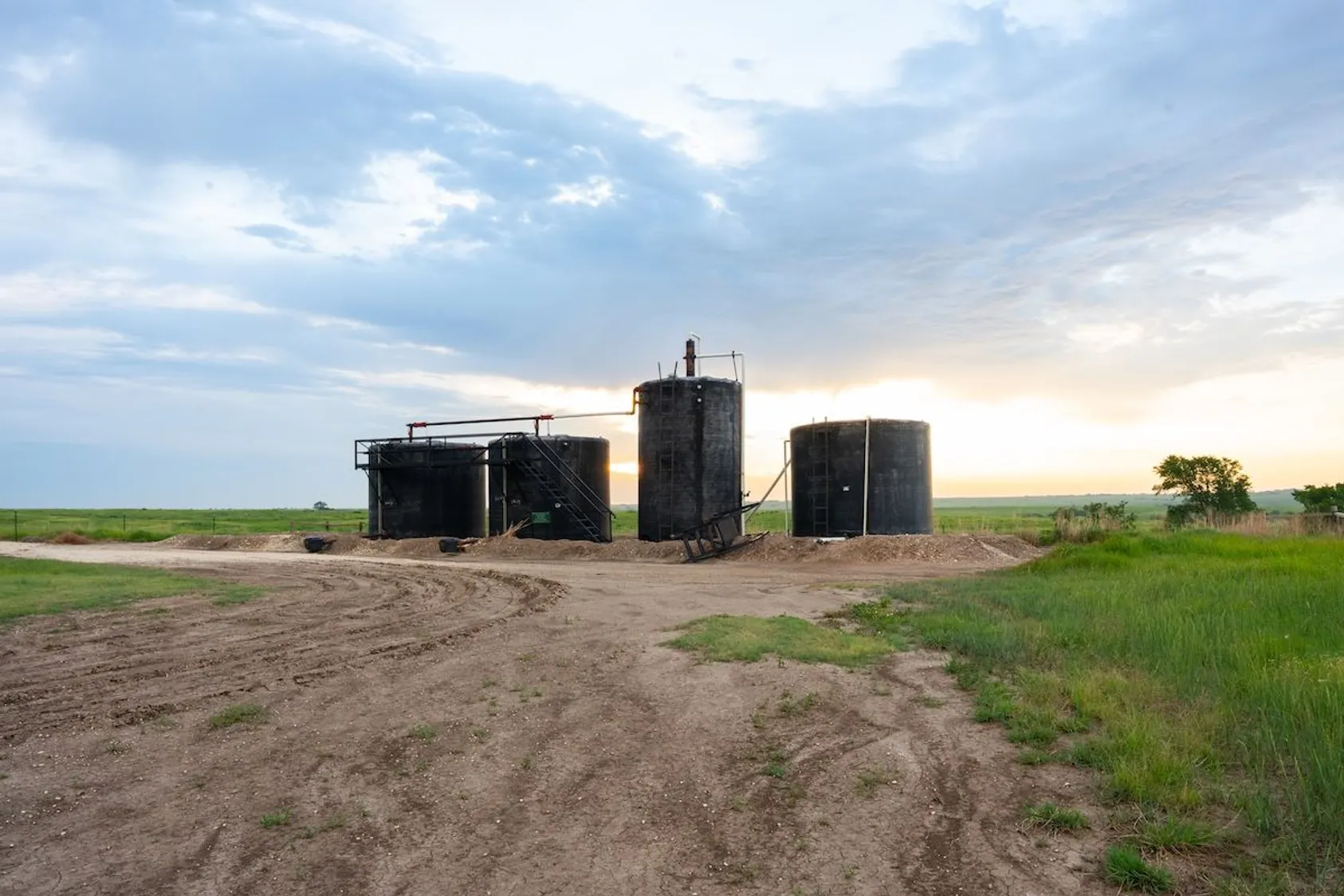 Three large cylindrical storage tanks on farmland, likely for oil or gas storage related to mineral extraction operations