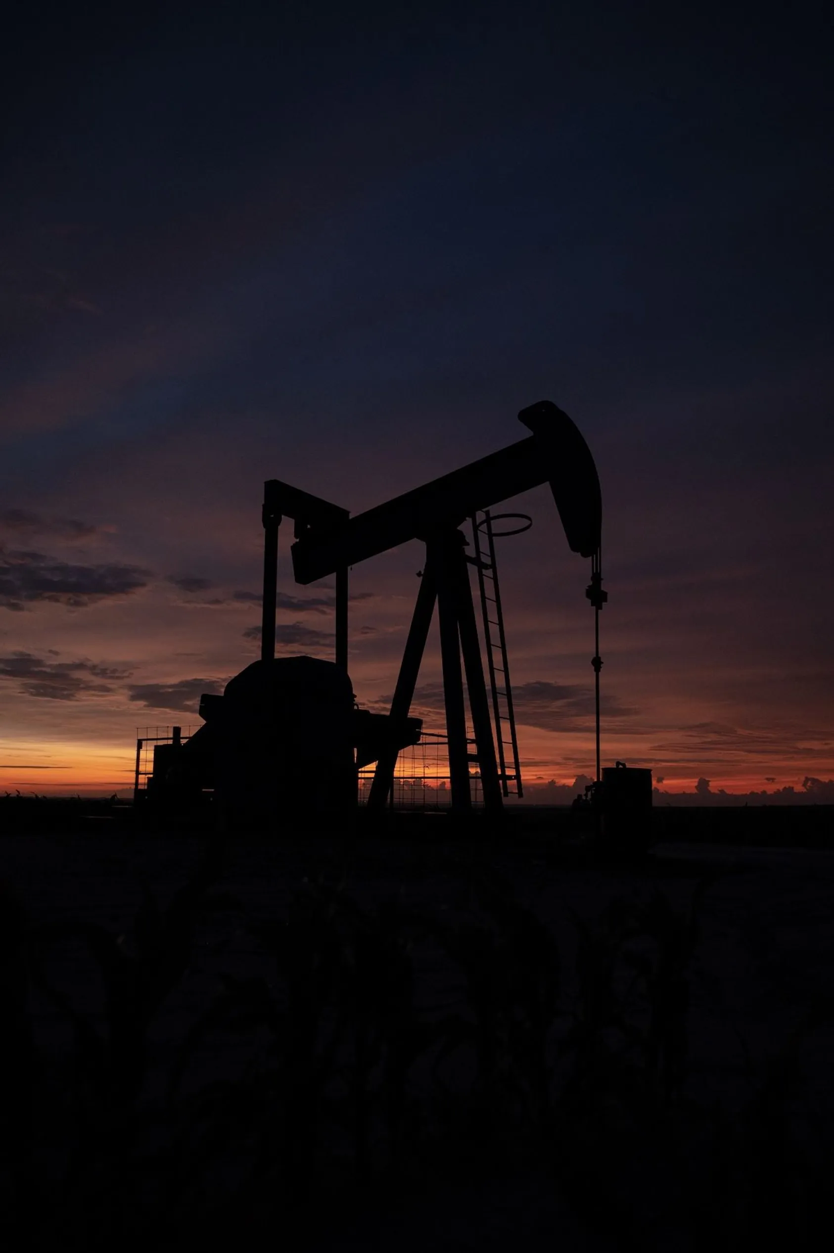 Silhouette of oil pump jack against sunset/sunrise sky, dramatically illustrating the oil extraction industry